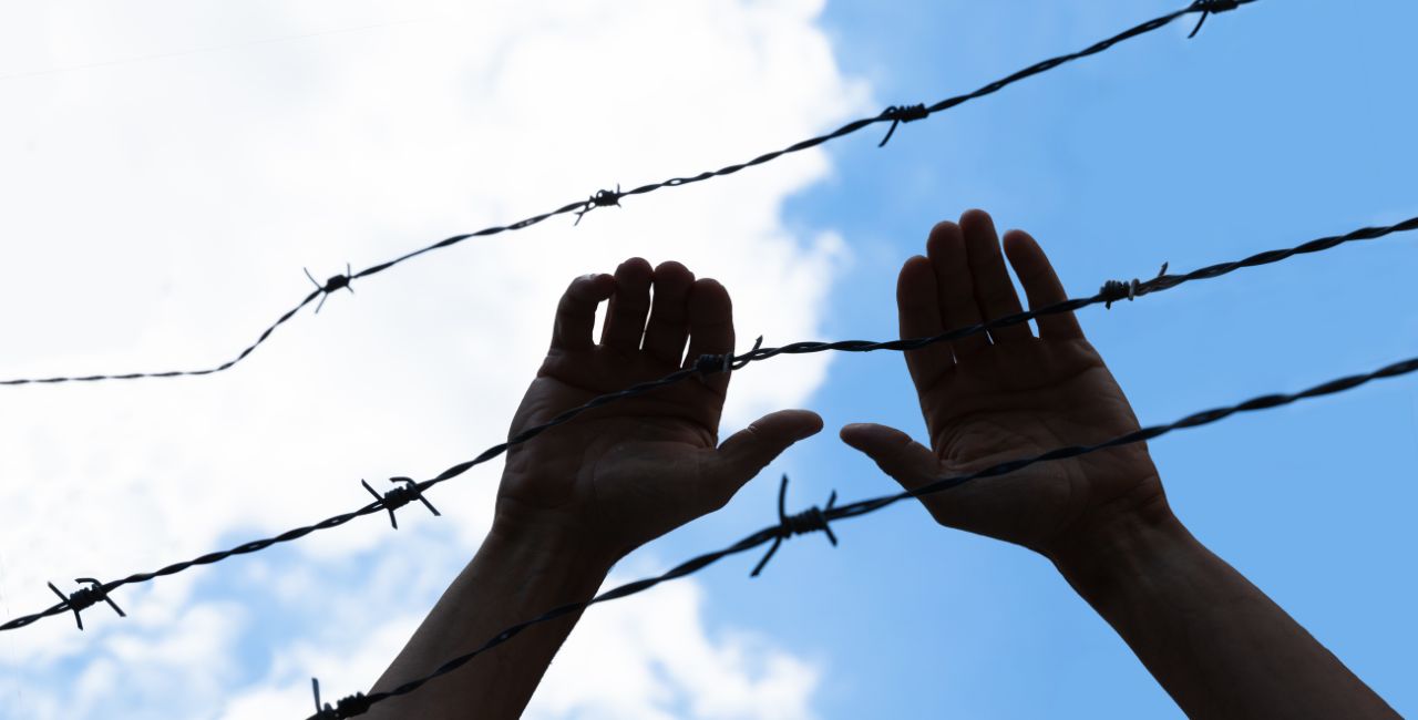 A person trying to climb over a barbed wire fence.