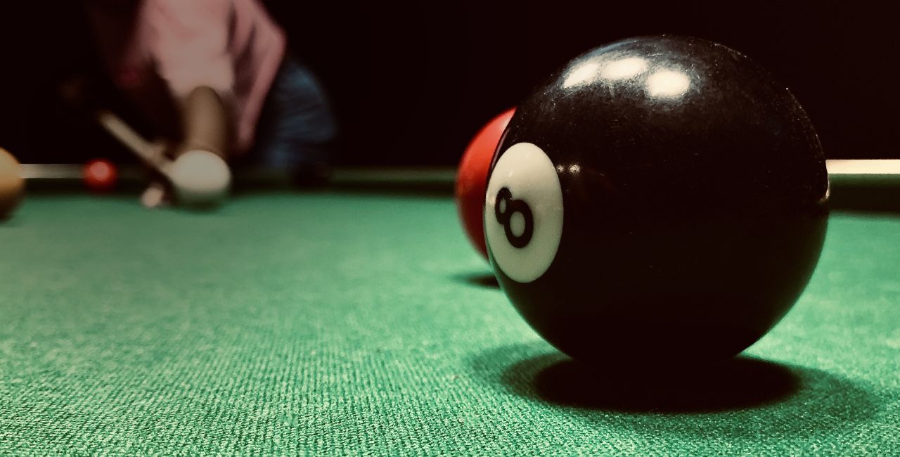 A person playing pool aiming at the eight ball.